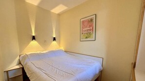 Ein Einzelbett in einem Zimmer mit Kopfteil, zwei Wandlampen und einem gerahmten Bild an der Wand.