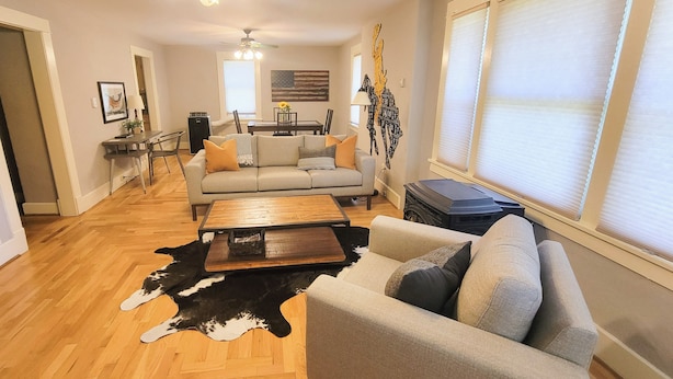 A spacious living room with a sofa, coffee table, and a dining area in the background. - Cottonwood Cottage- Walk to historic Downtown Cody, private yard (Cody)