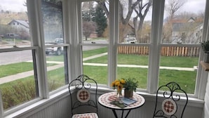 A corner room with two chairs and a small table, large windows with a view of a street and greenery. - Cottonwood Cottage- Walk to historic Downtown Cody, private yard (Cody)
