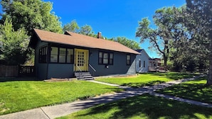 A residential house with a front yard, a pathway leading to the front door, and a neighboring house. - Cottonwood Cottage- Walk to historic Downtown Cody, private yard (Cody)