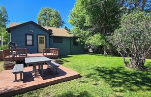 A blue house with a deck, a barbecue, and a picnic table.