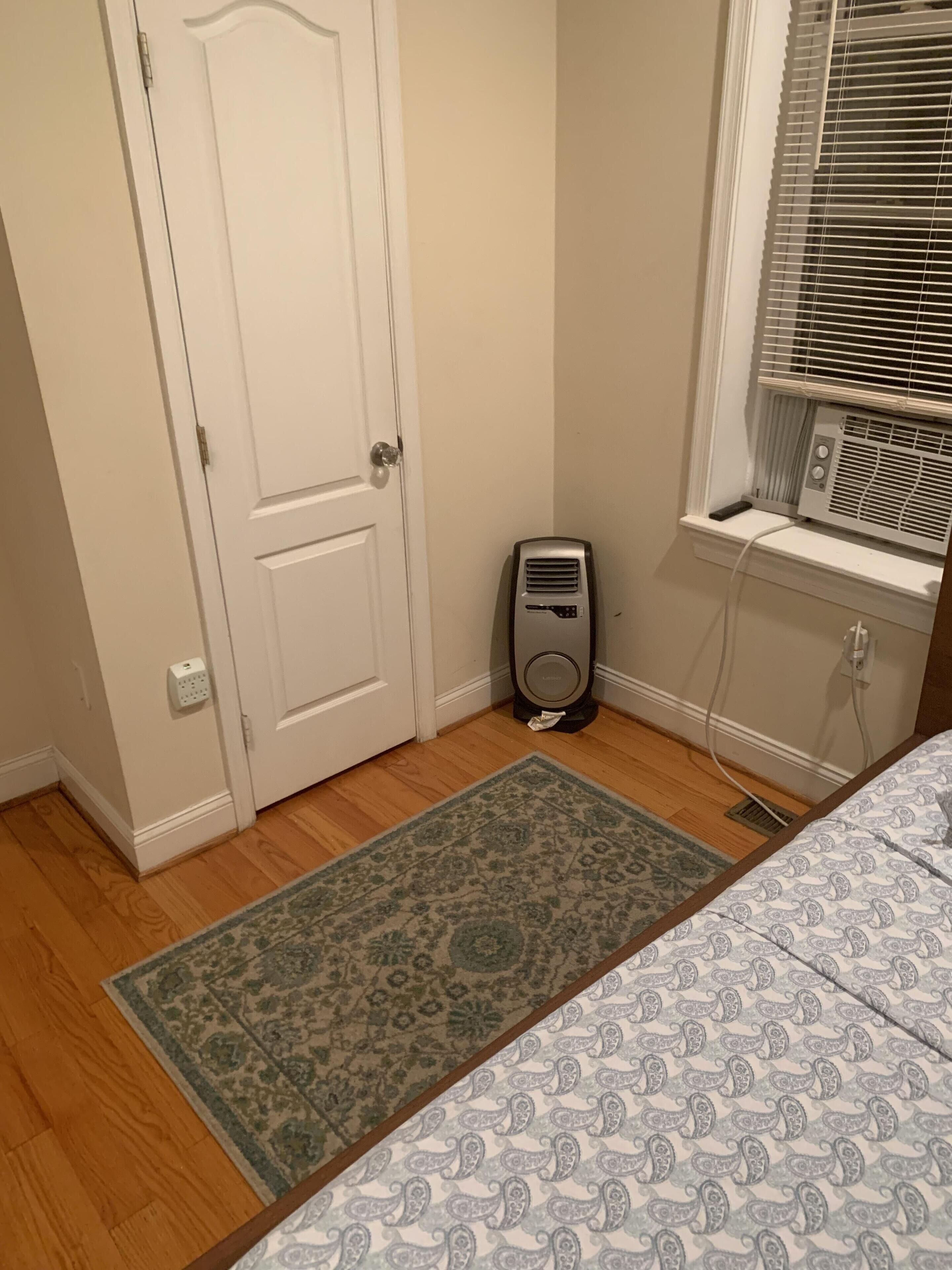 A bedroom with a bed, a window with blinds, a heater, and a door.