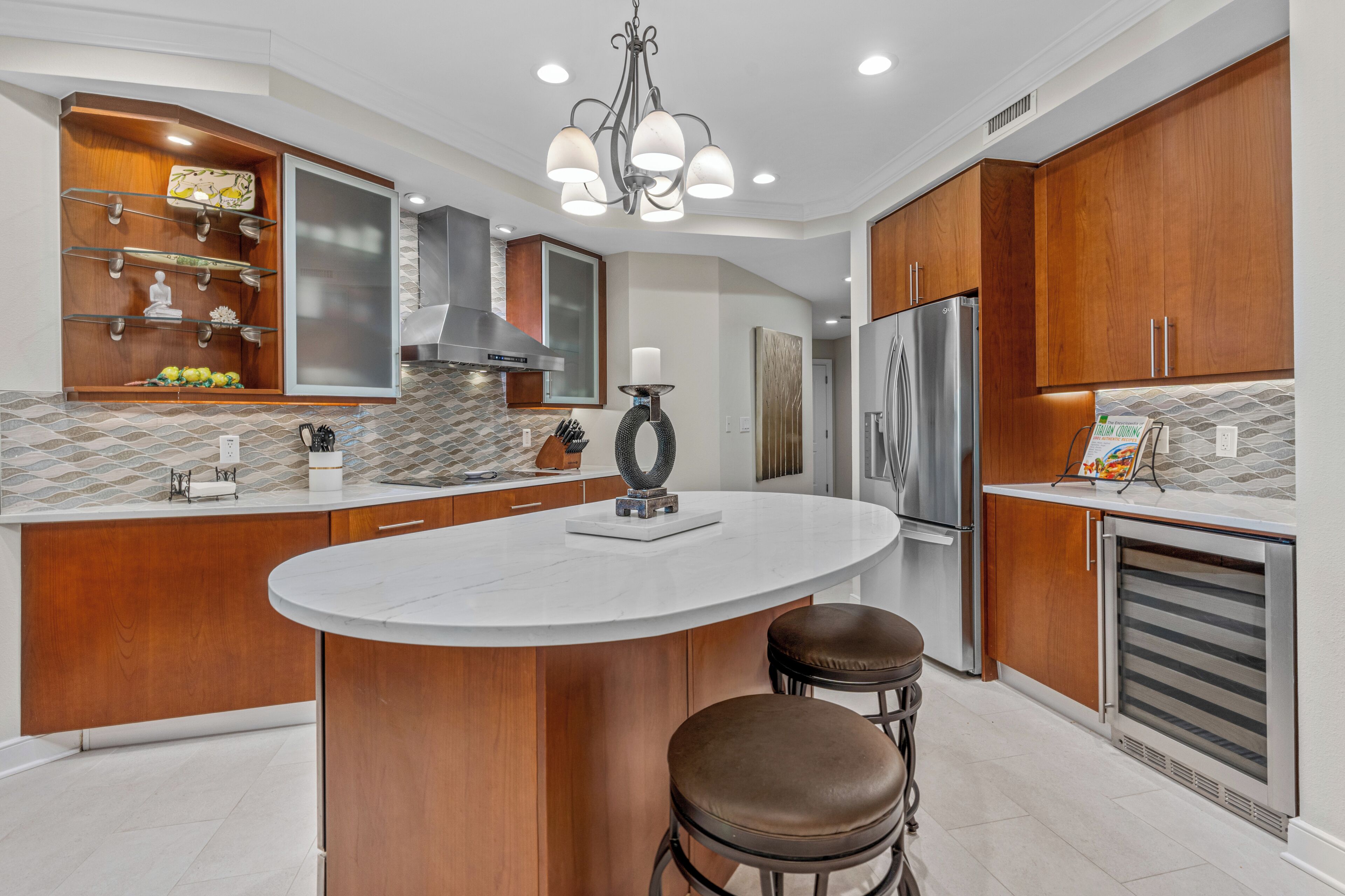 A modern kitchen with a central island, wooden cabinets, stainless steel appliances, and a chandelier.
