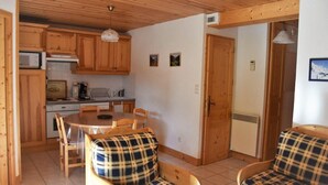 Una cocina acogedora con armarios de madera, una mesa de comedor y sillas. Hay un refrigerador pequeño, un microondas y un lavamanos.