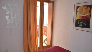 Un dormitorio con cama, ventana con cortinas, una obra de arte en la pared y vistas a un espacio exterior.