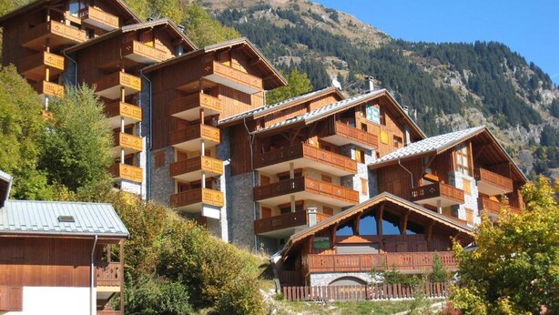 Una cabaña de madera de varios pisos con balcones, con montañas al fondo.