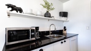 A compact kitchen with a microwave, coffee maker, sink, and white cabinets.