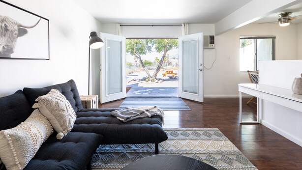 A modern living room with a dark sofa, a coffee table, and a view of an outdoor patio area.