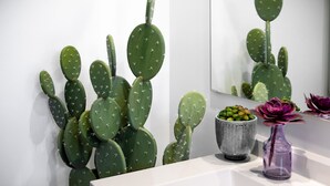 A bathroom with a white sink, a cactus wall, a small potted plant, and a mirror.