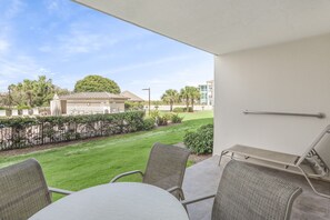 A balcony with a table and chairs, a view of a well-maintained lawn, and a building in the background.