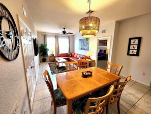 A dining area with a wooden table and chairs, a wicker chandelier, and a large wall clock. - Our Happy Place – Be our guest!  (Kissimmee)