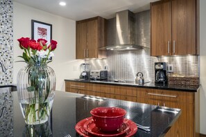 A modern kitchen with wooden cabinets, a stainless steel range hood, and a black countertop. - Walk to Thunderhead Lift! Hot Tub/ Pool! Quiet Building! (Steamboat Springs)