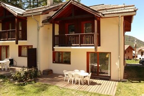 A two-story chalet with a balcony, a patio with outdoor seating, and a wooden deck.
