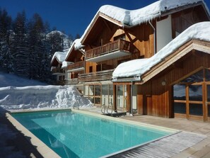 A wooden chalet with a pool, surrounded by snow-covered trees and a clear sky. - Chalet, ski-in/ski-out & foot of the slopes, swimming pool, sauna, hammam, terrace (Les Orres)