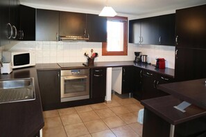 A modern kitchen with dark cabinetry, a stainless steel oven, a microwave, and a window providing natural light. - Chalet, ski-in/ski-out & foot of the slopes, swimming pool, sauna, hammam, terrace (Les Orres)