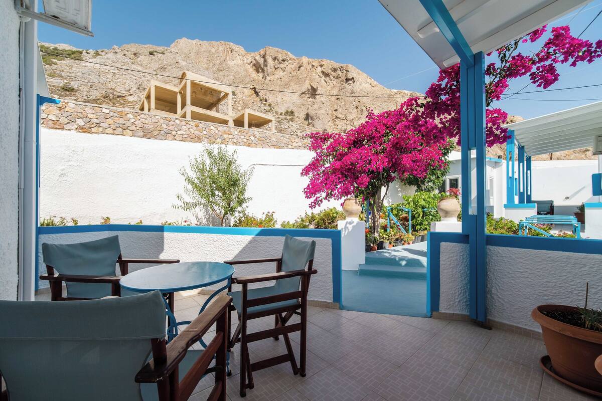 A terrace with outdoor seating, a view of a mountainous landscape, and a white building with blue accents.