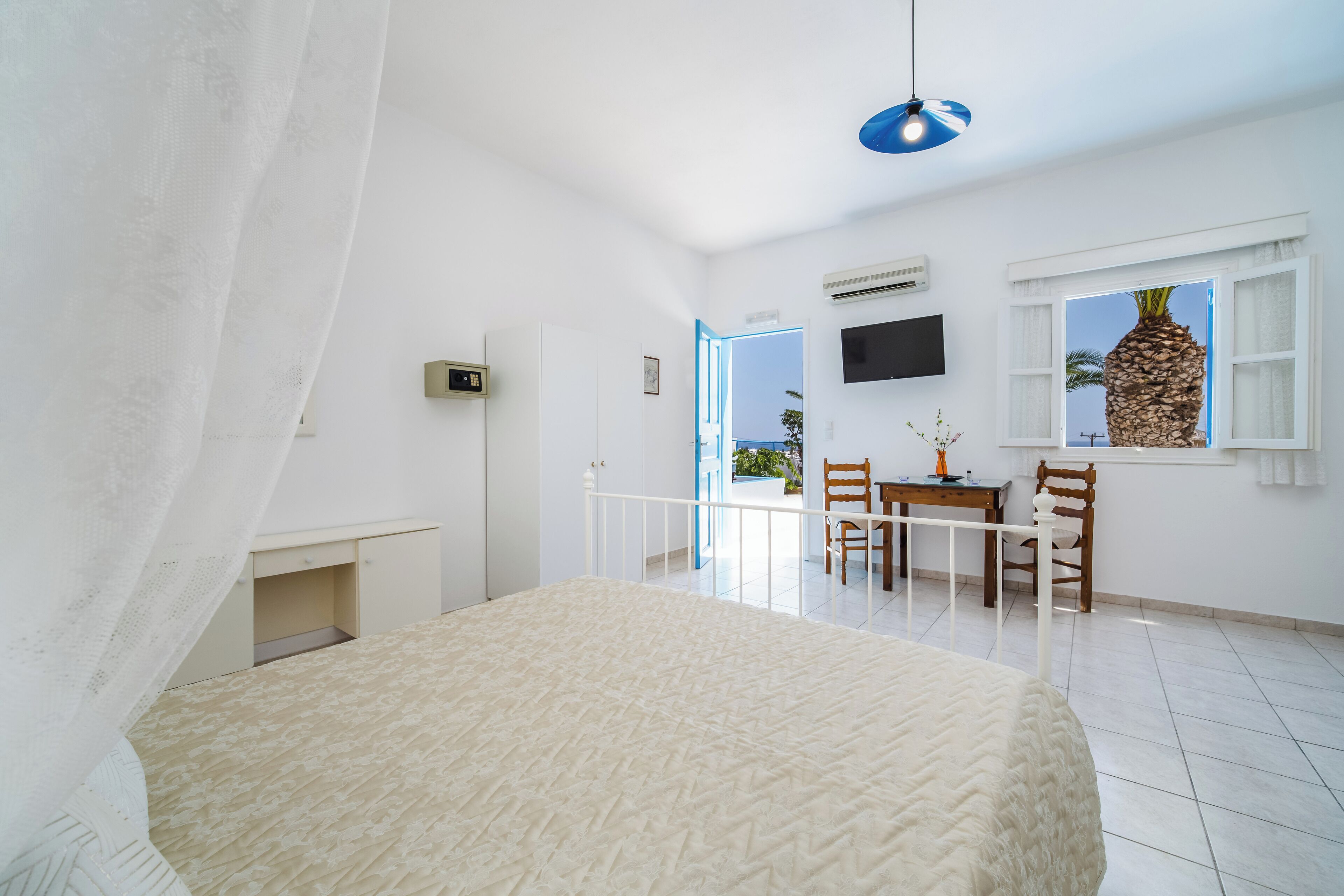 A bedroom with a bed, a desk, a chair, a TV, and a window with a view.