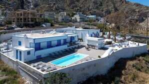 A coastal hotel with a rooftop pool, white and blue architecture, and a view of the surrounding rocky landscape. - Ancient Thera Apartments (Santorini)