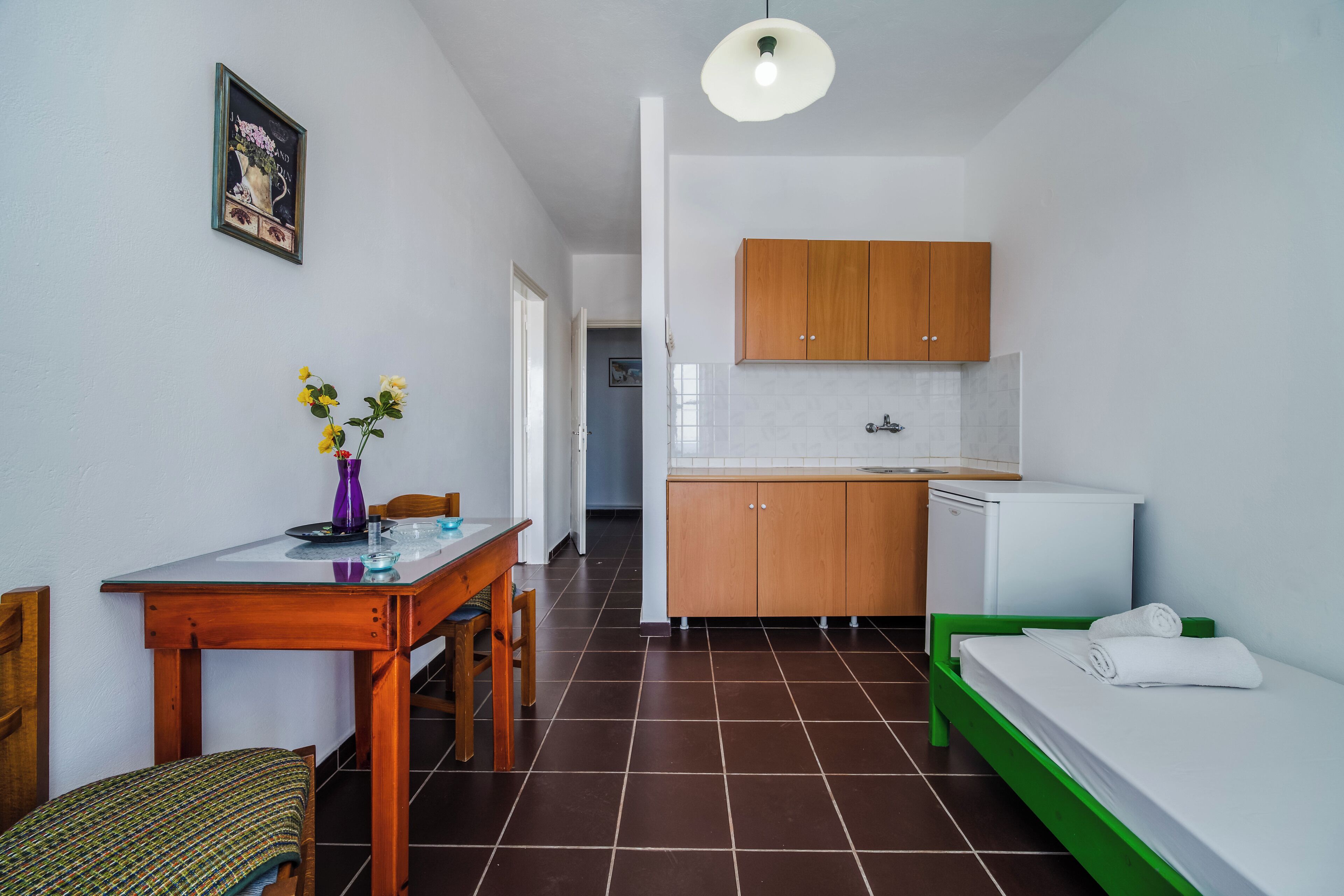 Ein kleines Zimmer mit Esstisch, einem grünen Bett, einer Küchenzeile und einem kleinen Badezimmer.