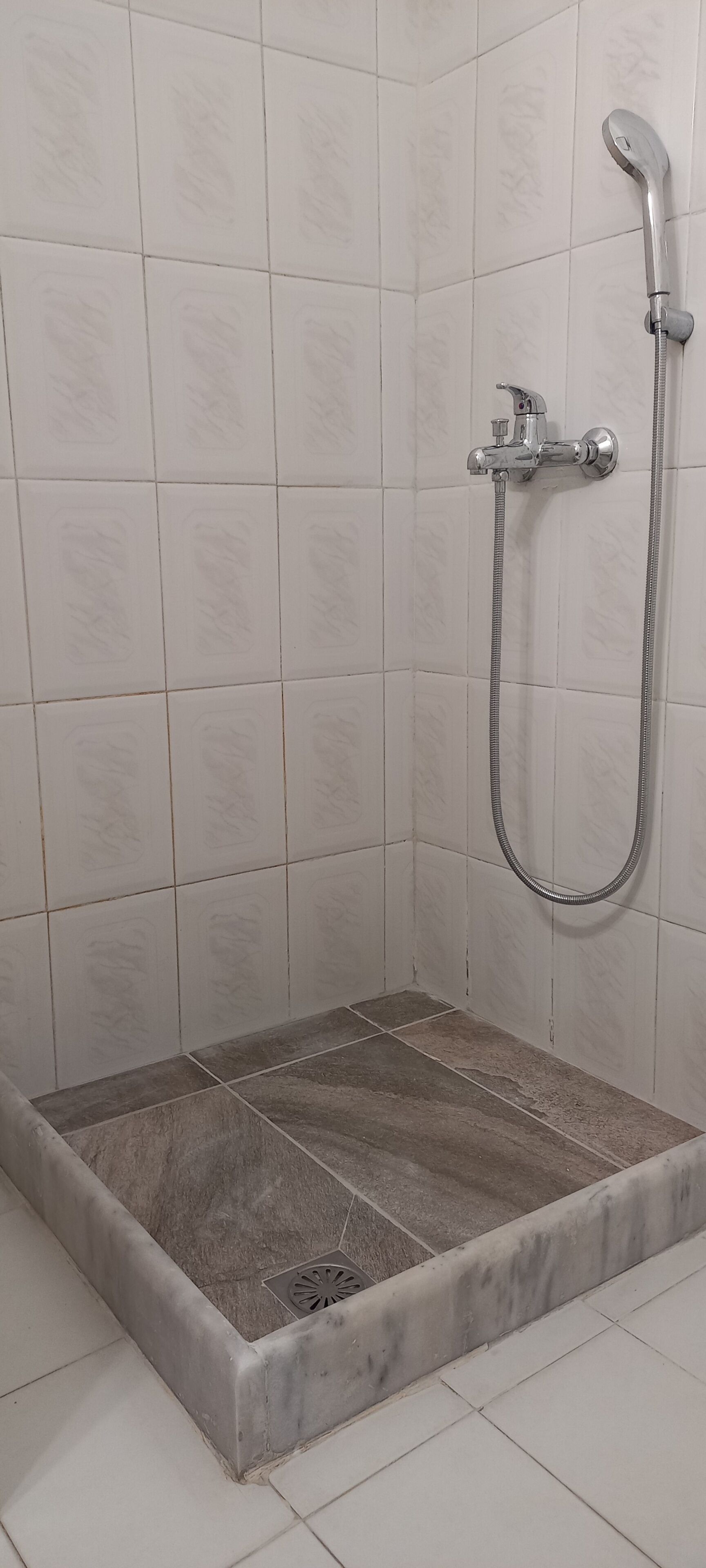 A shower area with a tiled wall, a showerhead, and a drain.