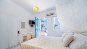 A bedroom with a bed, a TV, a balcony, and a view of the sea. - Ancient Thera Apartments (Santorini)