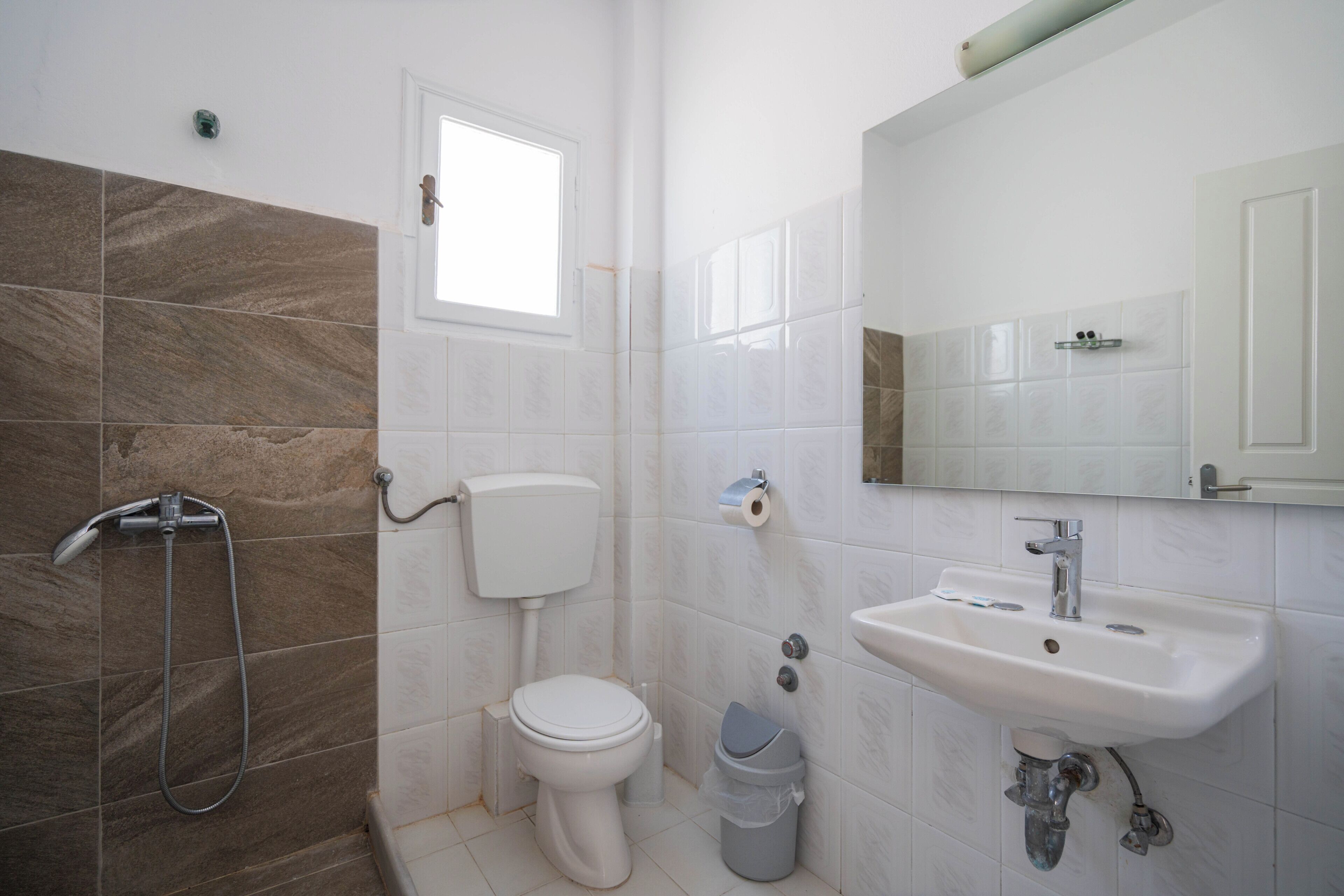 A bathroom with a shower, toilet, sink, and a small window.
