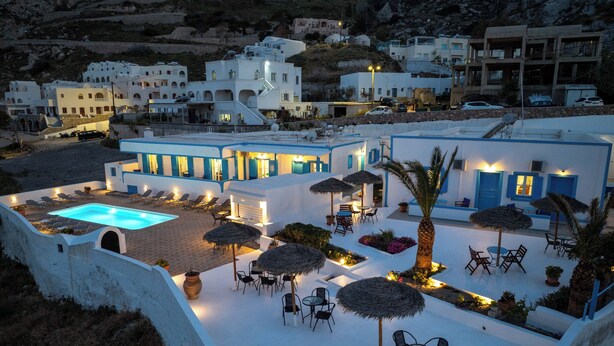 A resort with a swimming pool, outdoor seating, and a mountainous backdrop. - Ancient Thera Apartments (Santorini)