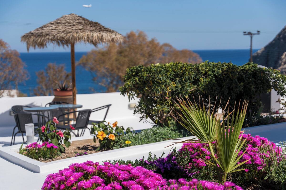 A patio with a table and chairs, a thatched umbrella, and a view of the sea.