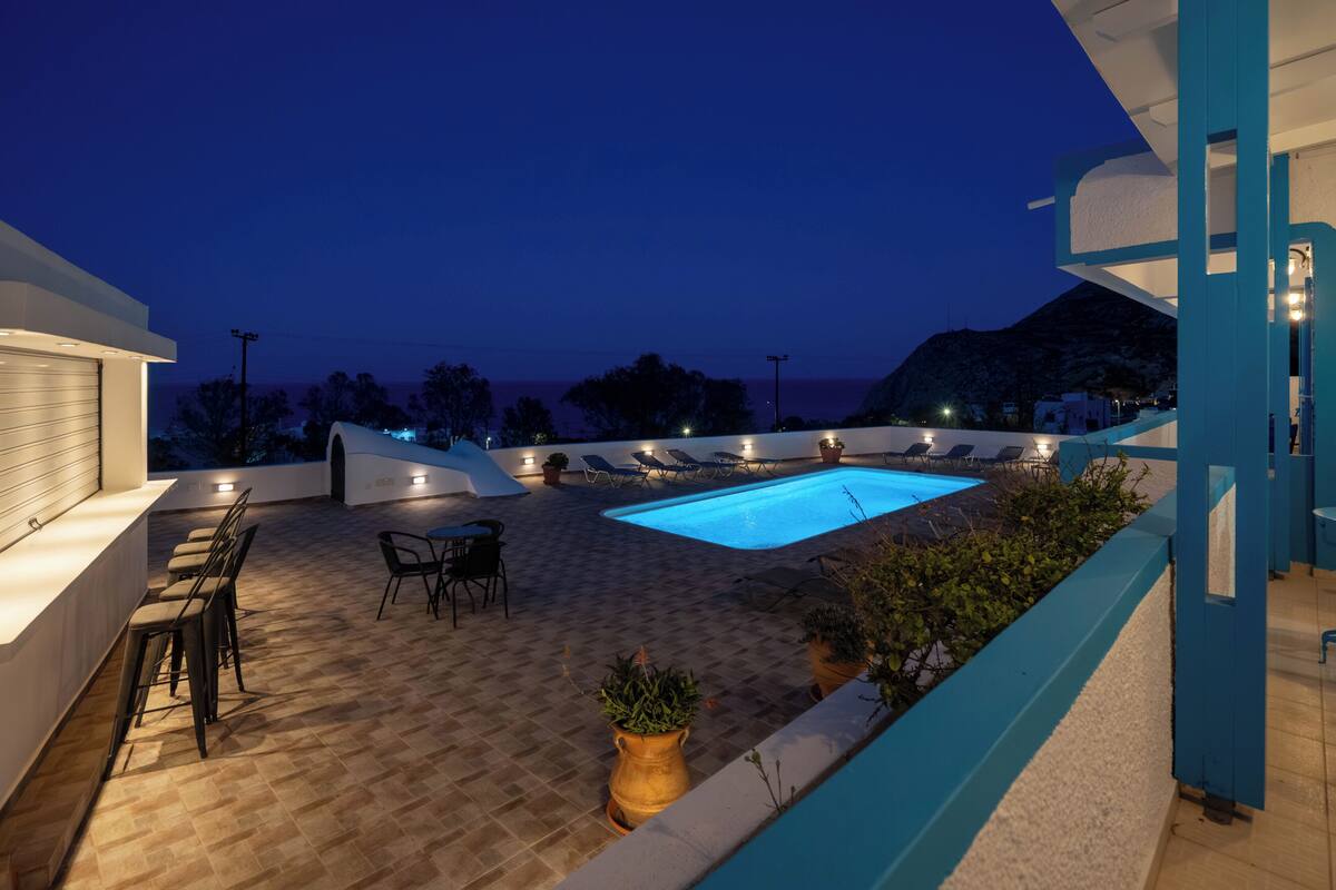A rooftop pool area with lounge chairs, a bar, and a view of the sea.