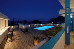 A rooftop pool area with lounge chairs, a bar, and a view of the sea. - Ancient Thera Apartments (Santorini)