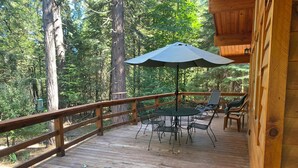 A wooden deck with a table and chairs, surrounded by a railing and overlooking a forest. - Cozy and comfortable wooded cabin (Alta)