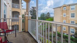 En balkon med en rød stol og gelænder i hvidt, der giver udsigt over en have og tilstødende bygninger.