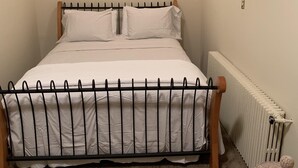 A bed with a metal frame and white bedding, a radiator, and a small woven basket on the floor.