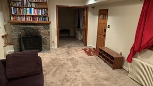 A living room with a stone fireplace, a bookshelf, a red curtain, and a radiator.