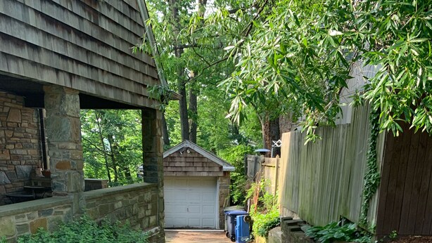 A narrow concrete pathway leading to a garage with a stone wall on one side and a wooden fence on the other.