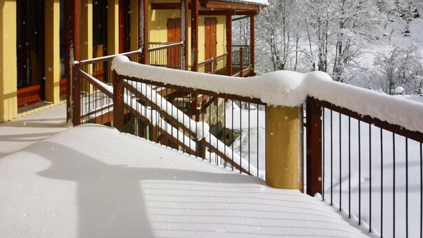 Un bâtiment enneigé doté d’une terrasse en bois et d’un escalier menant à un balcon.
