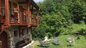 Un bâtiment en pierre doté d’un balcon en bois, d’une terrasse et, en arrière-plan, d’une colline verdoyante.