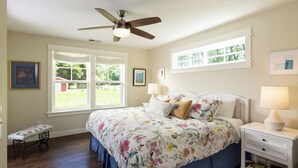 Um quarto com cama, mesas de cabeceira, ventilador de teto e janela.