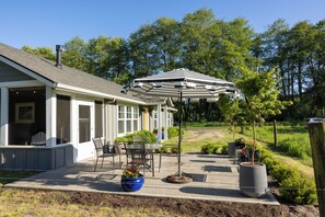 Une terrasse couverte, aménagée avec du mobilier d’extérieur, un grand parasol et des plantes en pot.