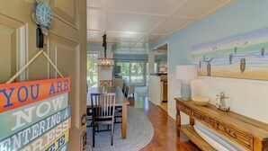 A dining area with a table and chairs, a wooden console table with a lamp, and a painting of seagulls on the wall. - Golf View, Pool, Pickleball, Stocked kitchen - 52 Fairway Dunes (Isle Of Palms)