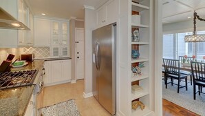 A kitchen with white cabinetry, a stainless steel refrigerator, and a dining area with a chandelier. - Golf View, Pool, Pickleball, Stocked kitchen - 52 Fairway Dunes (Isle Of Palms)