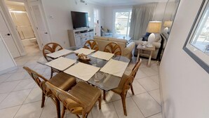 Un coin repas avec une table en verre, des chaises en bois et un téléviseur en arrière-plan.