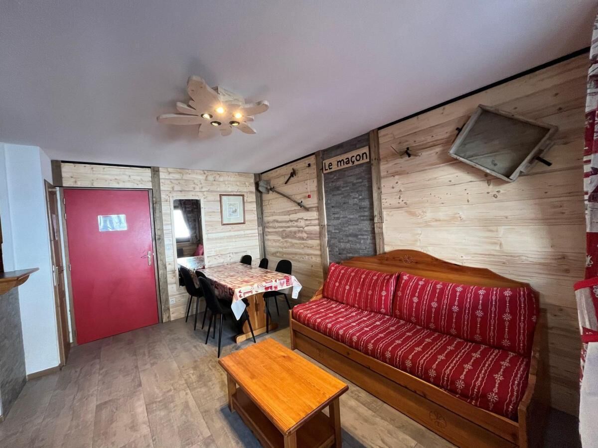 Une pièce chaleureuse avec une porte rouge, un canapé en bois, une table et un coin repas avec des chaises.