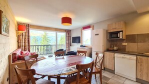 A cozy room with a wooden dining table, chairs, a sofa, a TV, a kitchen area with a microwave, and a window with curtains. - 150m from ski lifts, 3rd floor, balcony, tv, ski locker, 60m², Flaine (Flaine)