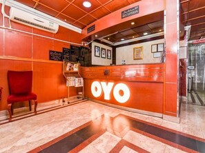 A reception area with a red chair, a reception desk with the name 'OYO' illuminated, and a sign for the 'Family Restaurant'. - Melody Queen Hotel (Dubai)