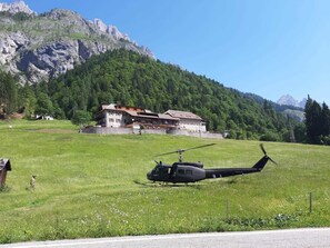 A helicopter parked on a grassy field with a mountain and a building in the background.