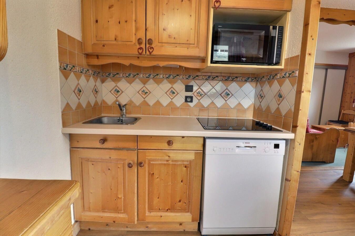 A compact kitchen with wooden cabinets, a microwave, a Bosch dishwasher, and a tiled backsplash.