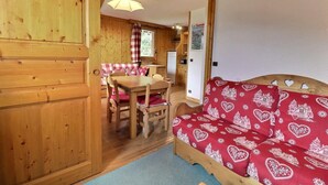 A wooden interior with a dining area, a sofa with a red patterned cover, and a kitchen visible in the background. - 250m from ski slopes, 4th floor, balcony, 38m², Méribel-Mottaret (Méribel - Les Allues)