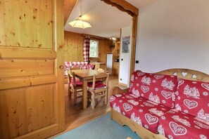A wooden interior with a dining area, a sofa with a red patterned cover, and a kitchen visible in the background. - 4th floor, balcony, 38m², Méribel-Mottaret (Méribel - Les Allues)