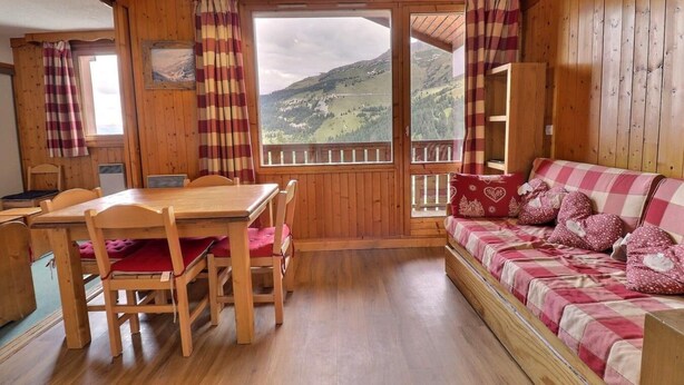A wooden cabin interior with a dining table, chairs, a sofa, and a view of a mountainous landscape through large windows. - 250m from ski slopes, 4th floor, balcony, 38m², Méribel-Mottaret (Méribel - Les Allues)